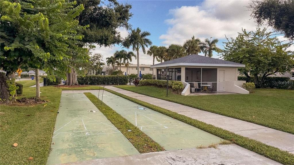 An outdoor shuffleboard court sits on a lawn next to a small, screened-in community pavilion — 7461 W COUNTRY CLUB DRIVE N UNIT 306, SARASOTA, FL