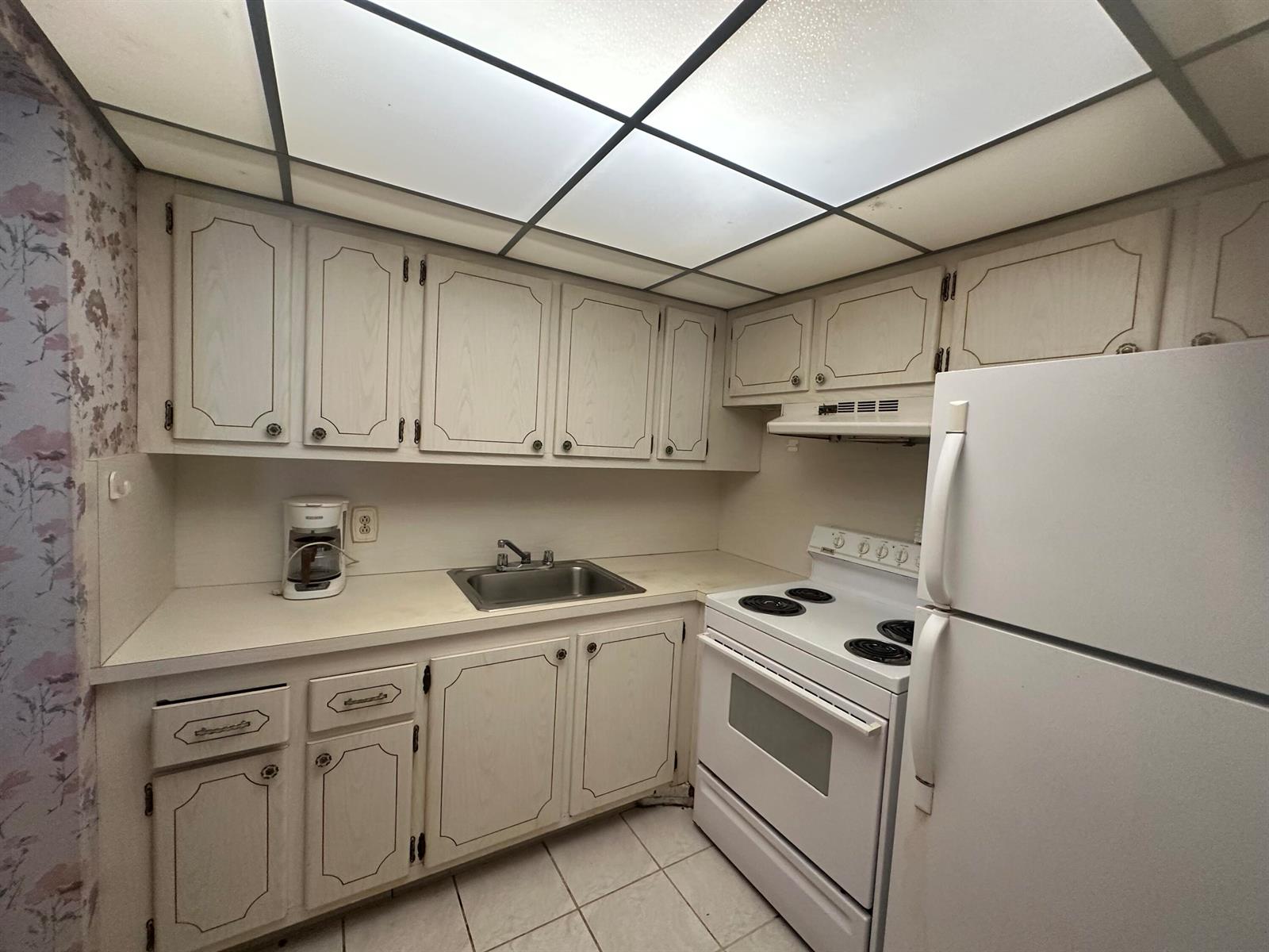 A kitchen features white cabinets, a white stove, a refrigerator, and a drop ceiling — 72 Northampton D, West Palm Beach FL 33417, WEST PALM BEACH, FL