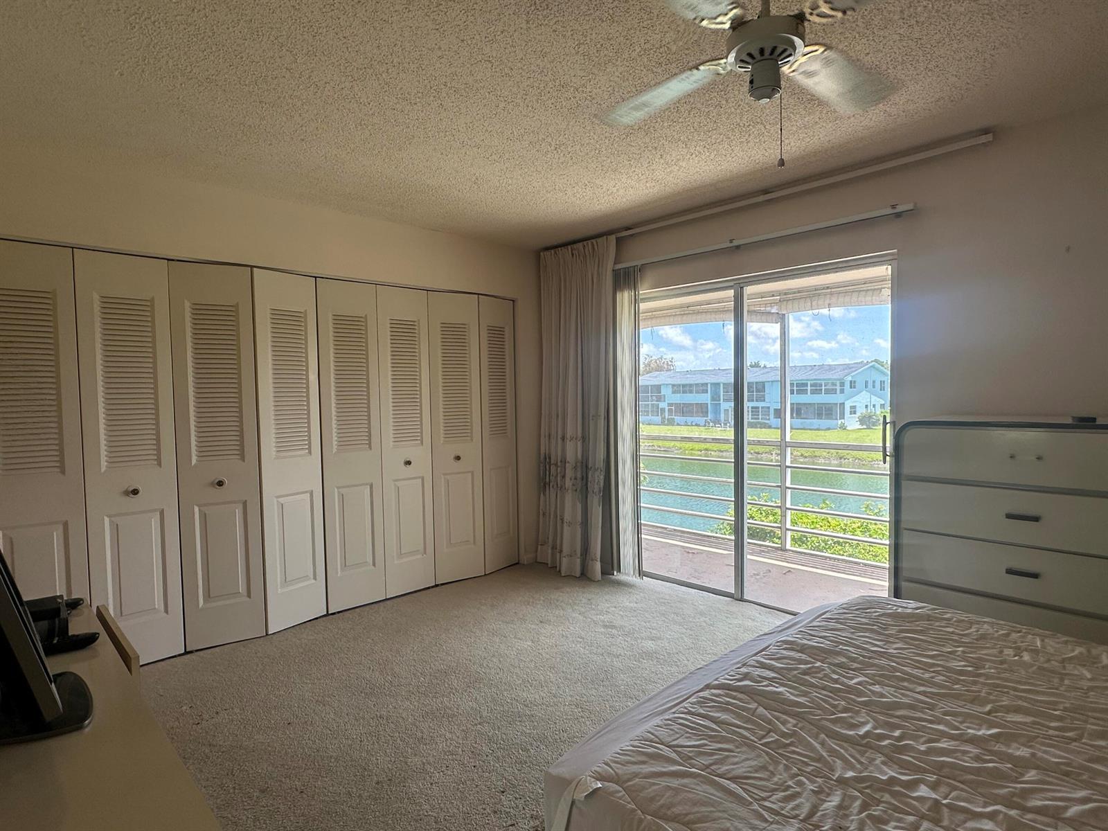 A bedroom with beige carpet, a large louvered closet, and a sliding door to a balcony — 72 Northampton D, West Palm Beach FL 33417, WEST PALM BEACH, FL