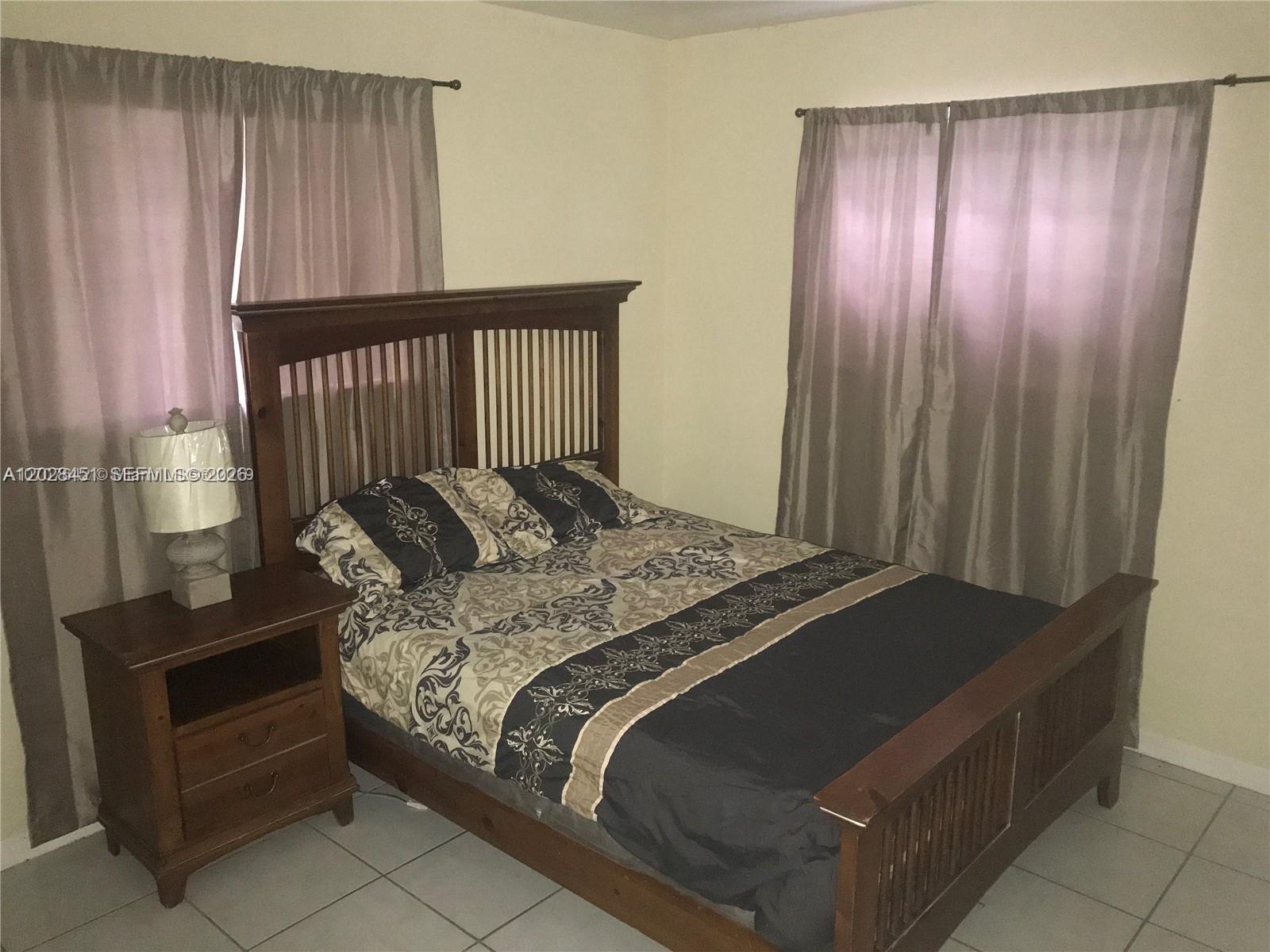 A bedroom features a wooden bed frame, a matching nightstand, and curtains over two windows — 133 NW 57th St # 2, Miami FL 33127, MIAMI, FL