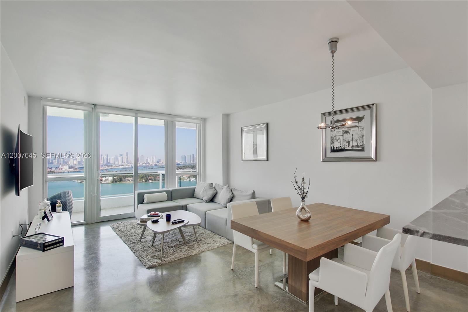A modern living and dining area features concrete floors, a sectional sofa, and floor-to-ceiling windows — 540 West Ave # 2112, Miami Beach FL 33139, MIAMI BEACH, FL