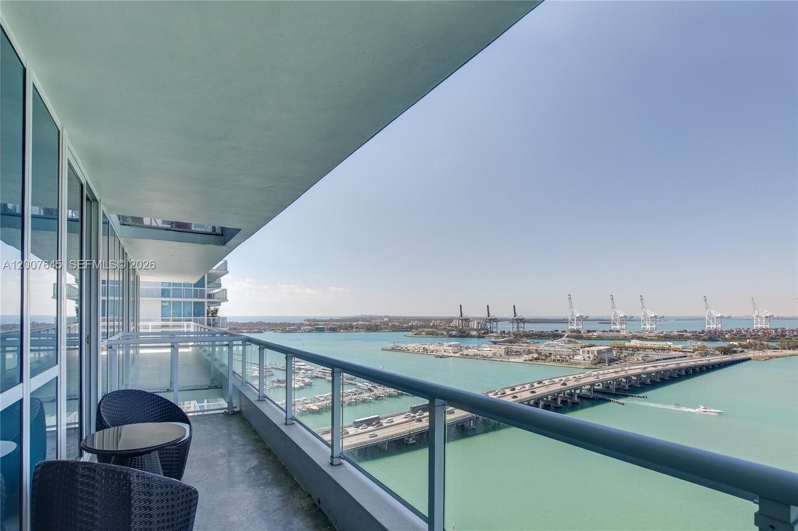 A balcony with outdoor seating overlooks a bridge, a marina, and a shipping port — 540 West Ave # 2112, Miami Beach FL 33139, MIAMI BEACH, FL