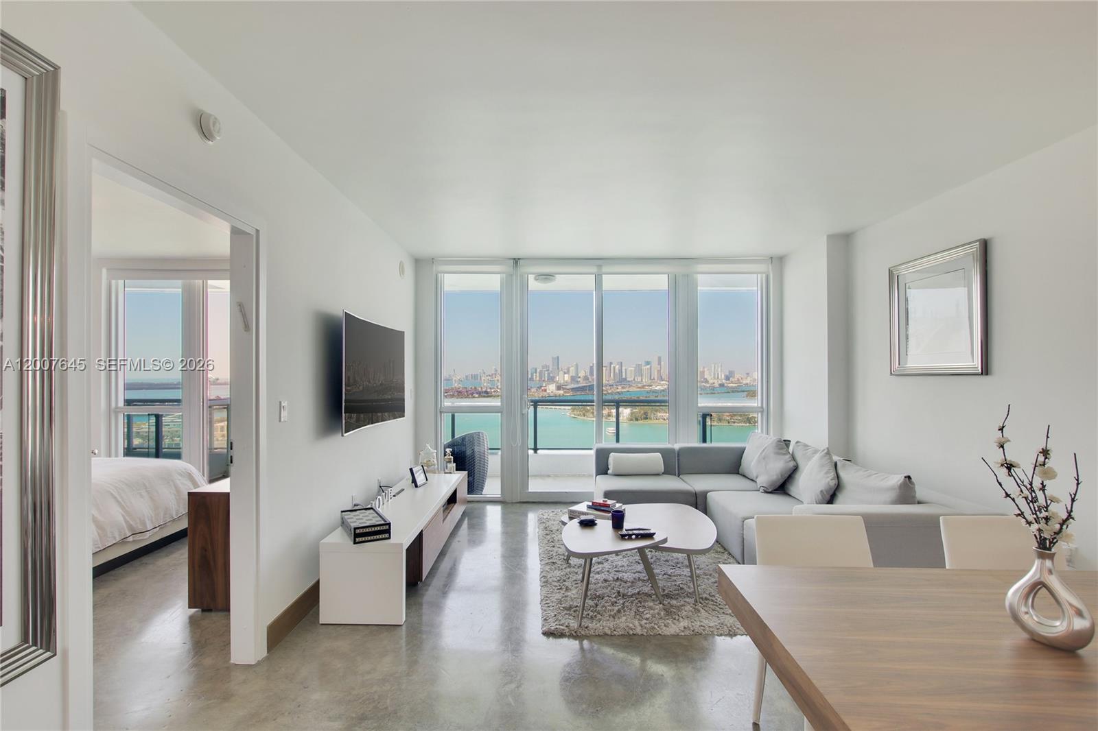 A modern living room features a grey sectional, white media console, and floor-to-ceiling city views — 540 West Ave # 2112, Miami Beach FL 33139, MIAMI BEACH, FL