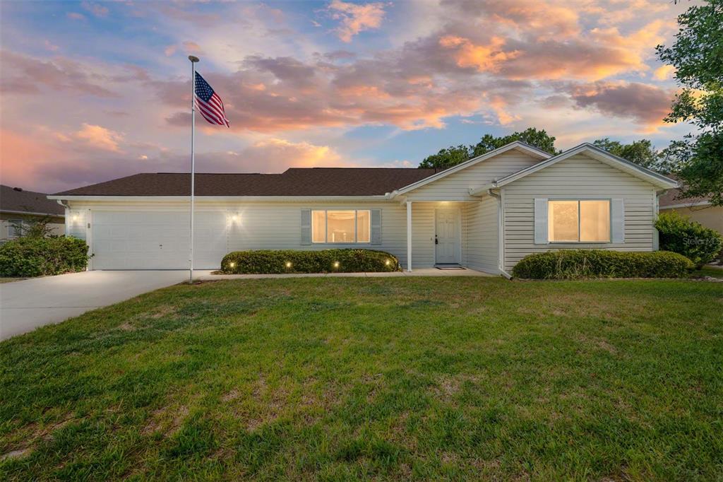 A single-story house with light siding, a two-car garage, and an American flag in front — 11587 SW 139TH PLACE, DUNNELLON, FL