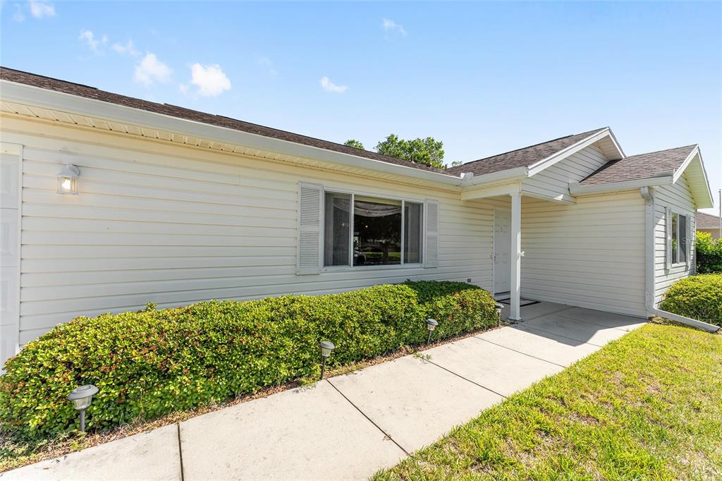A beige vinyl-sided house exterior features a concrete walkway leading to a covered front entrance — 11587 SW 139TH PLACE, DUNNELLON, FL