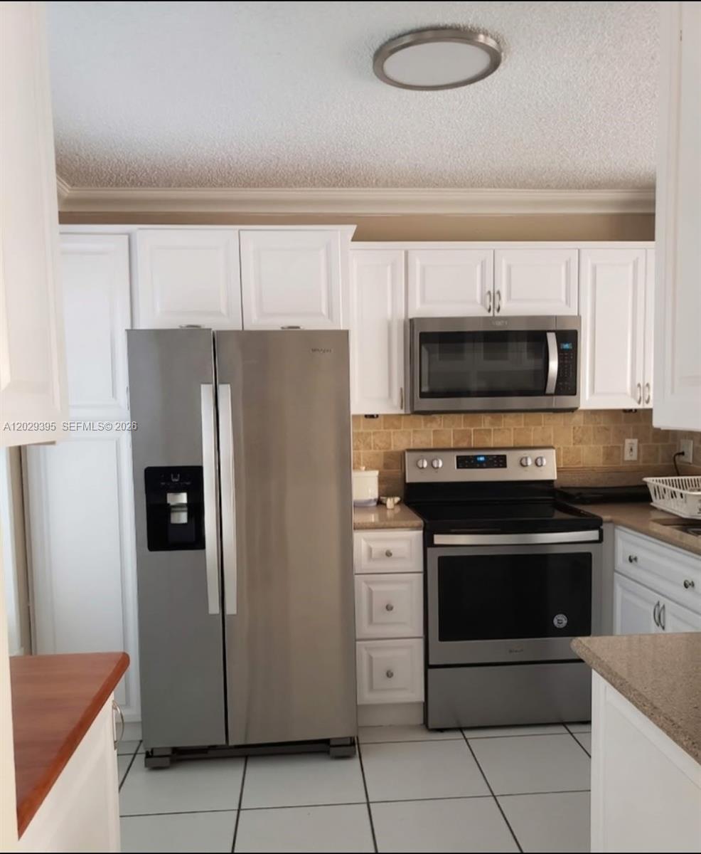 A kitchen features white cabinets, stainless steel appliances, a tiled backsplash, and light-colored countertops — 223 Maple Ter, Davie FL 33325, DAVIE, FL