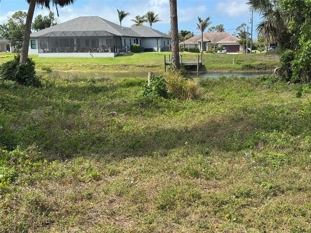 A grassy vacant lot sits in front of a canal and residential houses — 50 PINE VALLEY LANE, ROTONDA WEST, FL
