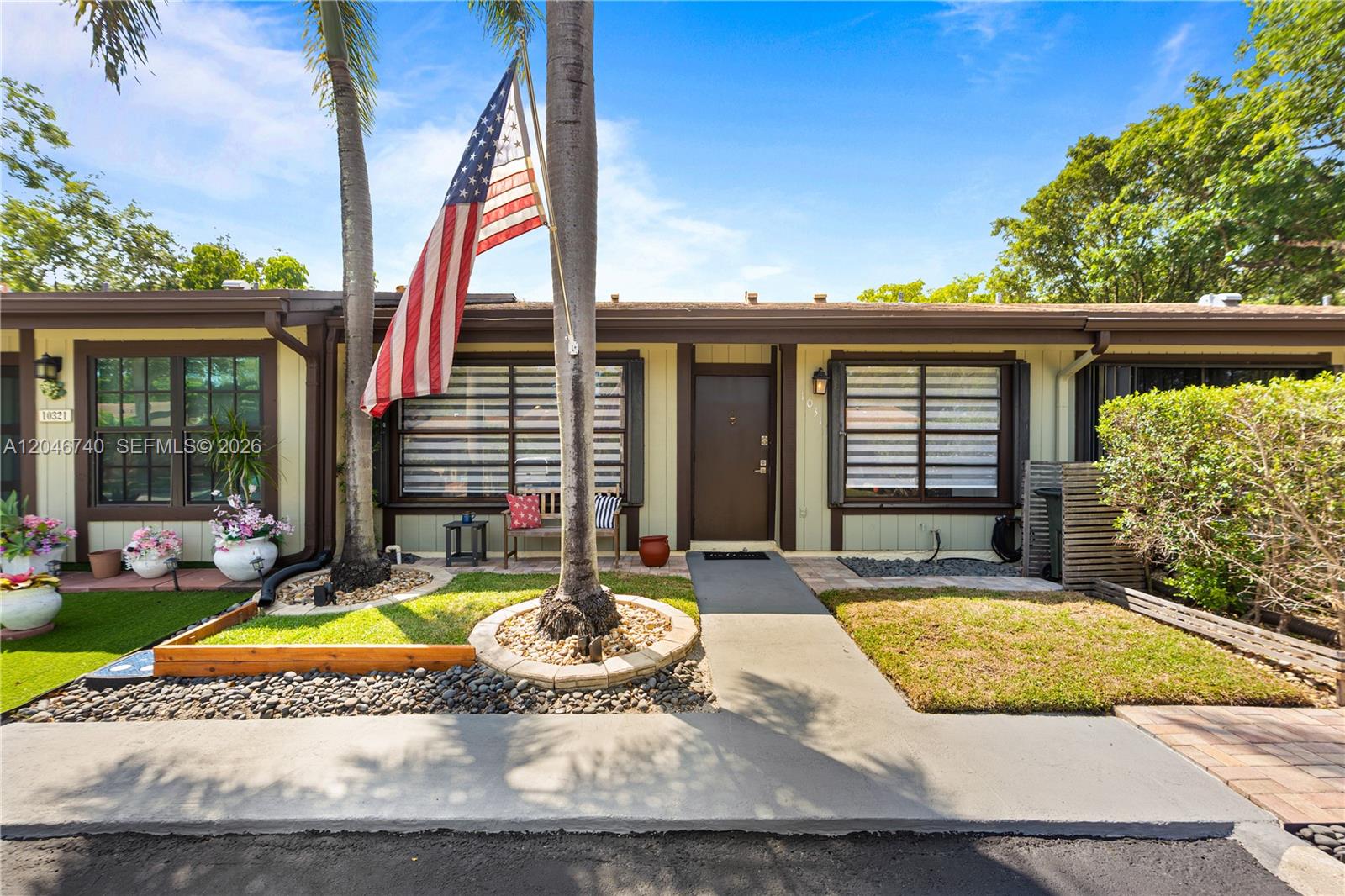 The exterior of a single-story home features a brown door, palm trees, and an American flag — 10311 Laurel Ct, Pembroke Pines FL 33026, PEMBROKE PINES, FL