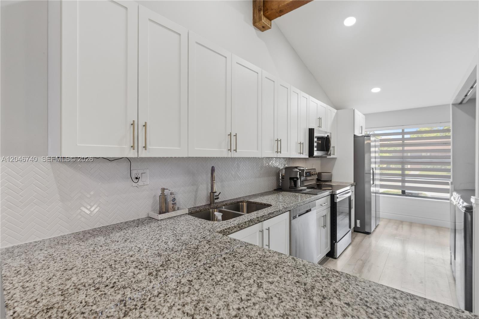 A kitchen features white cabinets, granite countertops, a herringbone backsplash, and a vaulted ceiling — 10311 Laurel Ct, Pembroke Pines FL 33026, PEMBROKE PINES, FL
