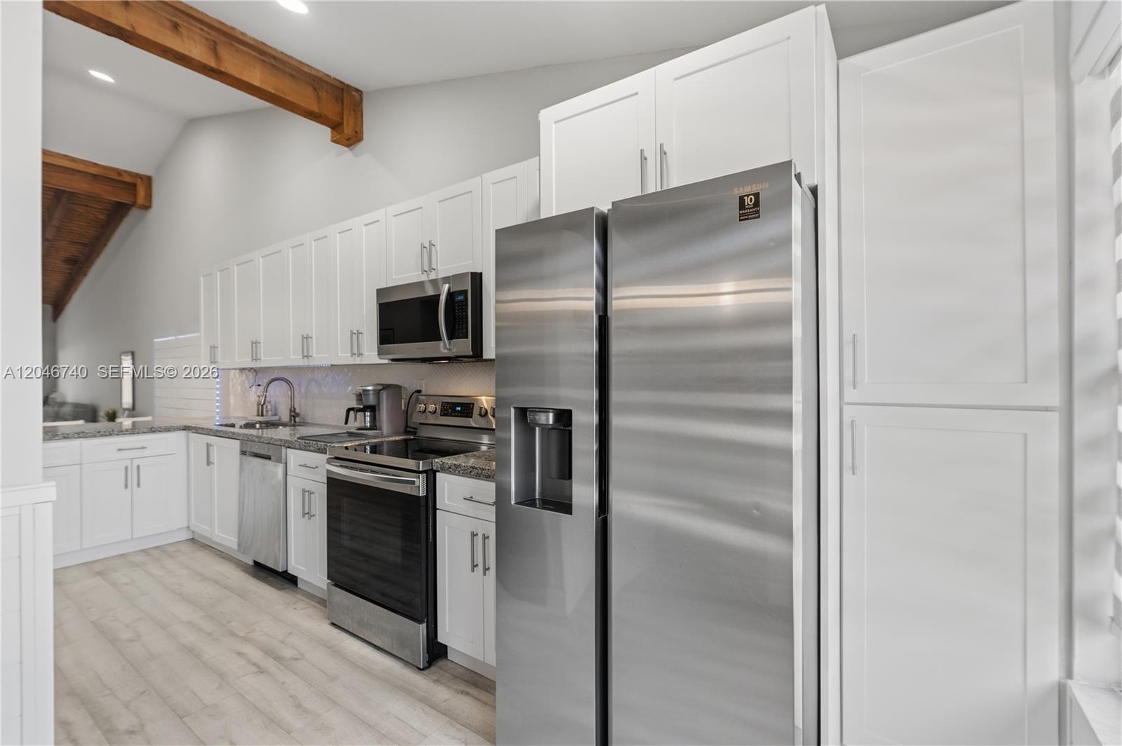 A modern kitchen features white shaker cabinets, stainless steel appliances, and exposed wooden ceiling beams — 10311 Laurel Ct, Pembroke Pines FL 33026, PEMBROKE PINES, FL