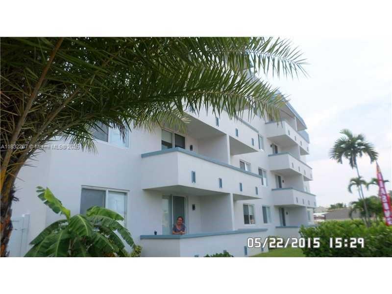 A multi-story white apartment building features balconies and palm trees under a cloudy sky — 11750 NE 16th Ave # 102, Miami FL 33161, MIAMI, FL