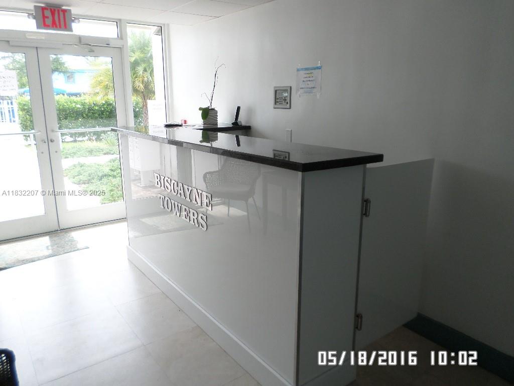 A white reception desk with a black countertop stands in a bright building lobby — 11750 NE 16th Ave # 102, Miami FL 33161, MIAMI, FL