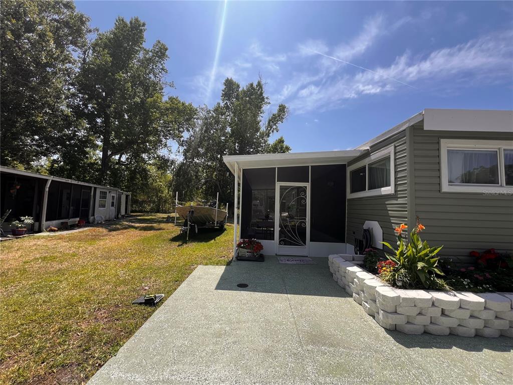 A concrete patio leads to a screened-in porch next to a house with gray siding — 7291 WINDY WAY, BROOKSVILLE, FL
