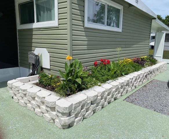 A raised stone garden bed sits against the side of a light green mobile home — 7291 WINDY WAY, BROOKSVILLE, FL