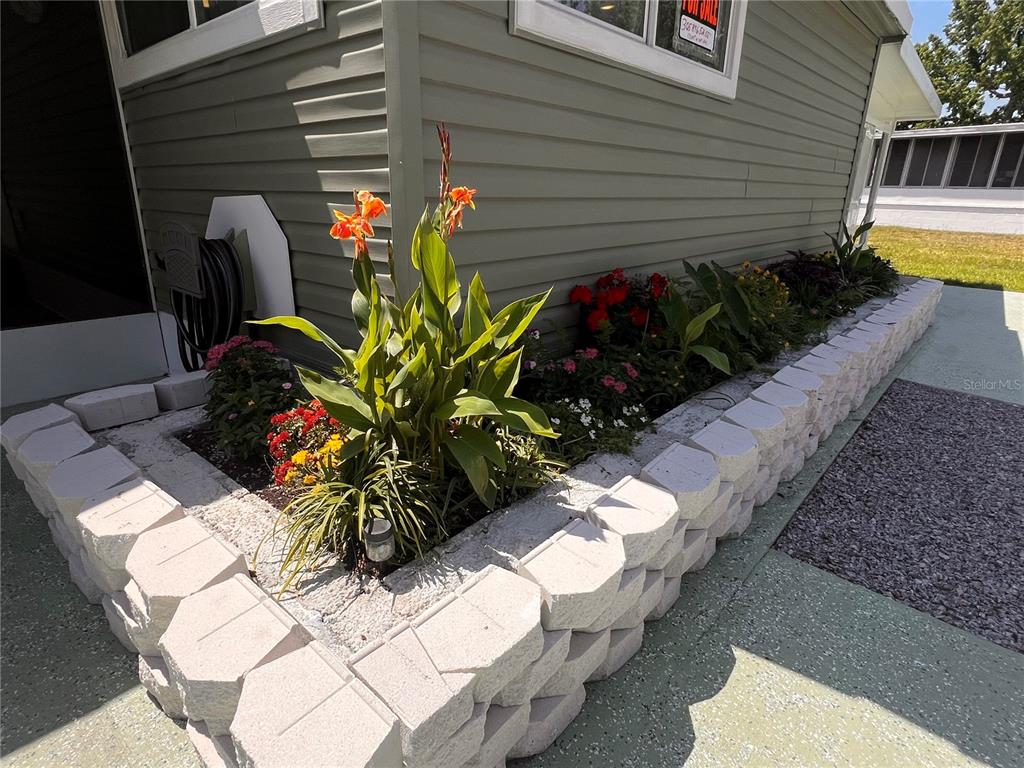 A raised stone garden bed sits in front of a house with light green siding — 7291 WINDY WAY, BROOKSVILLE, FL