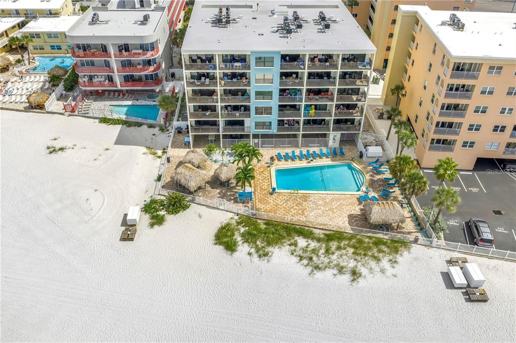 An aerial view shows a multi-story beachfront condominium building with a pool and parking lot — 12924 GULF BOULEVARD UNIT 510, MADEIRA BEACH, FL