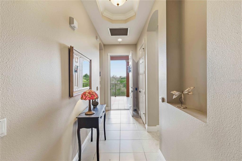 A tiled hallway leads to an open doorway revealing a balcony with a scenic outdoor view — 5246 MANORWOOD DRIVE UNIT 4C, SARASOTA, FL