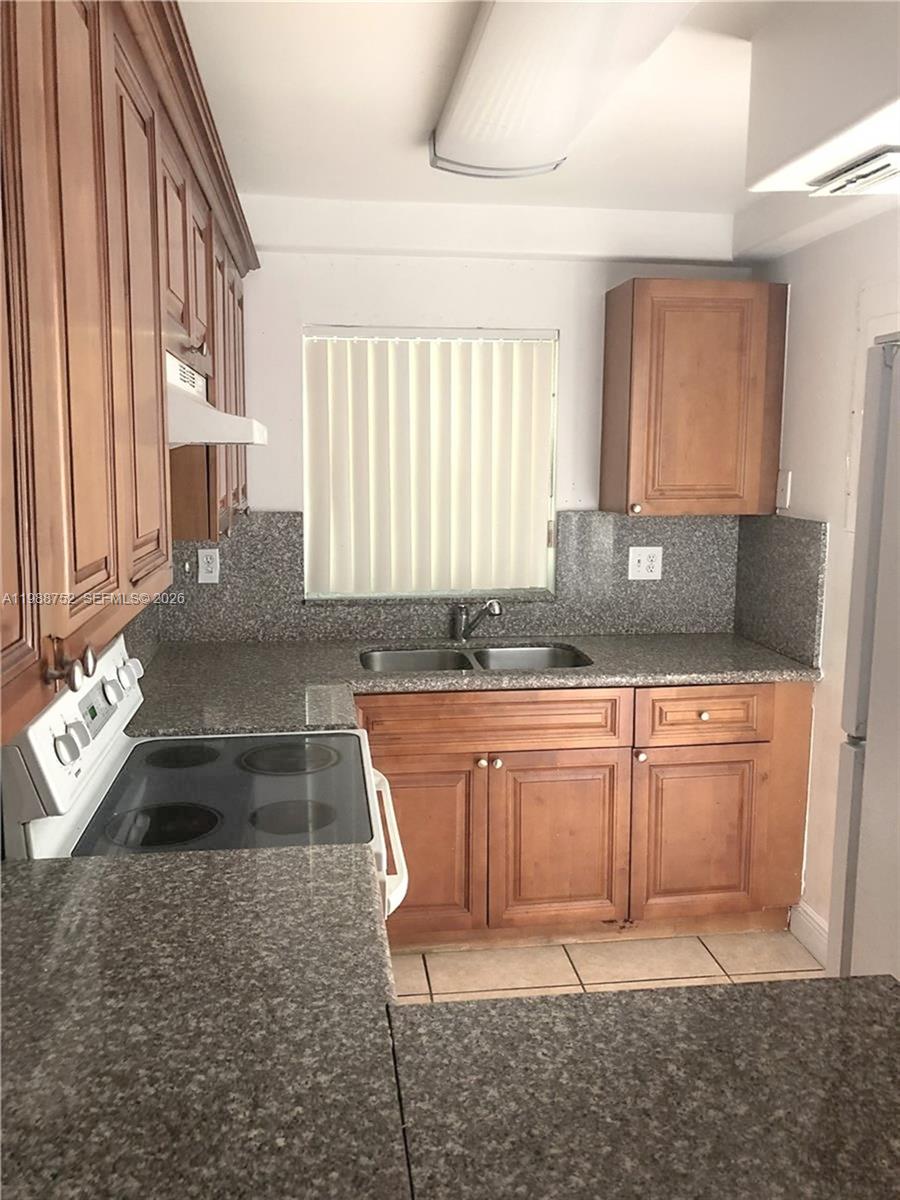 A kitchen features wood cabinets, granite countertops, a white stove, and a window with blinds — 4415 W 10th Ln # 14, Hialeah FL 33012, HIALEAH, FL