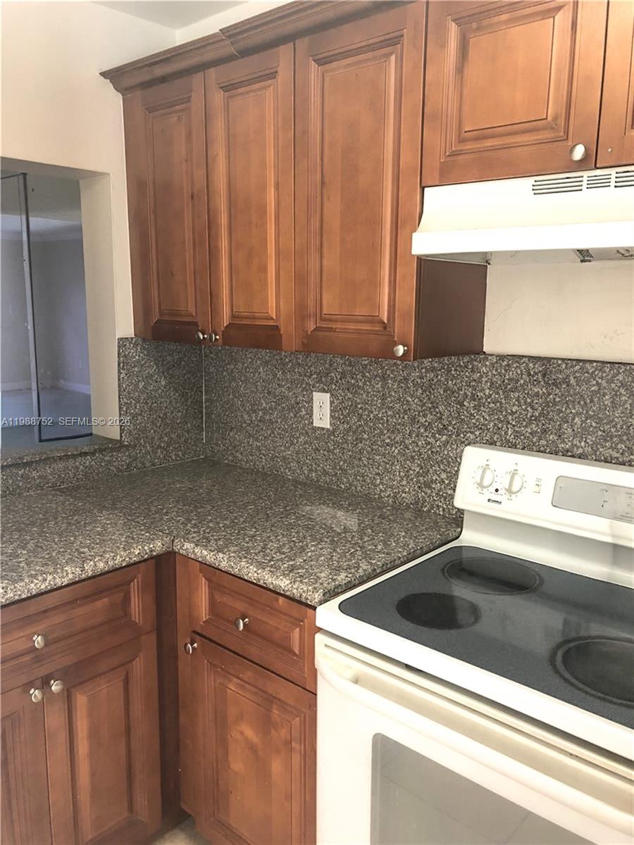 A kitchen features wood cabinets, a granite countertop, and a white electric stove — 4415 W 10th Ln # 14, Hialeah FL 33012, HIALEAH, FL