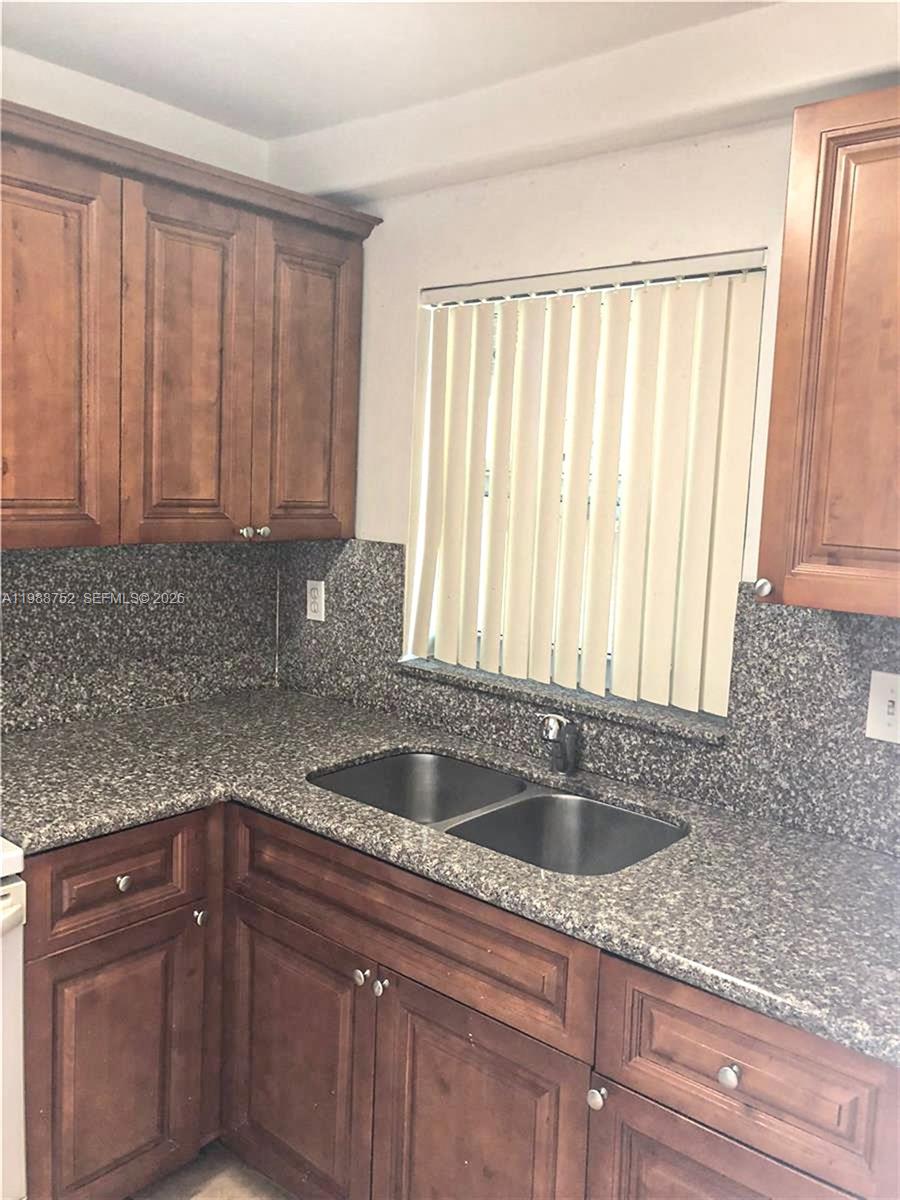A kitchen features wood cabinets, a granite countertop, and a double-basin sink under a window — 4415 W 10th Ln # 14, Hialeah FL 33012, HIALEAH, FL