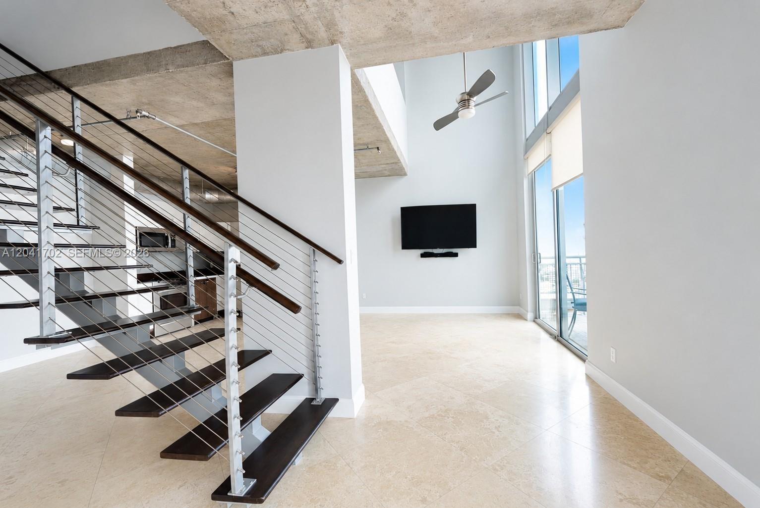 A modern living room features a floating staircase, concrete ceilings, and floor-to-ceiling windows — 690 SW 1st Ct # 3118, Miami FL 33130, MIAMI, FL