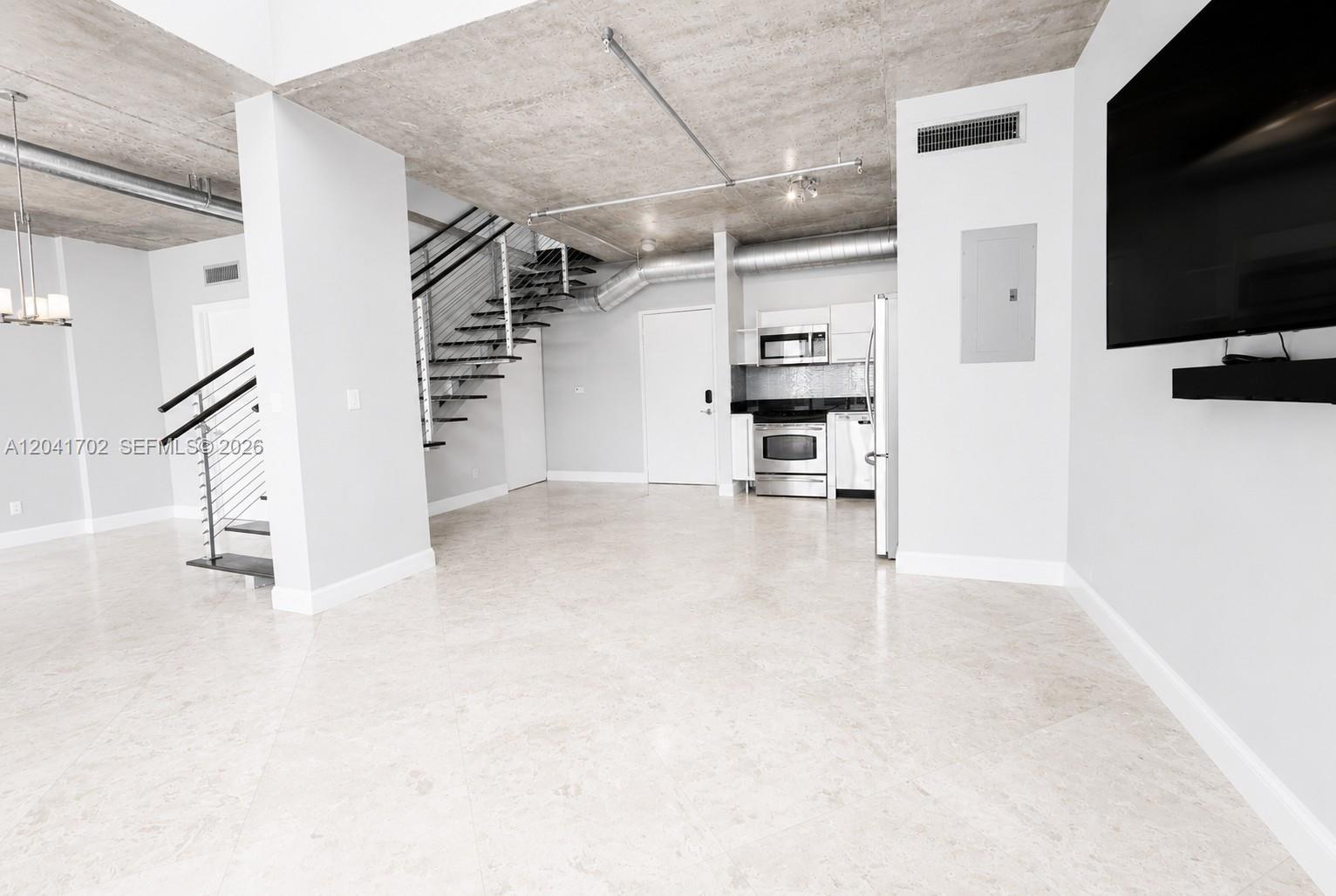 This open-concept living area features a concrete ceiling, tiled floors, and a metal staircase — 690 SW 1st Ct # 3118, Miami FL 33130, MIAMI, FL