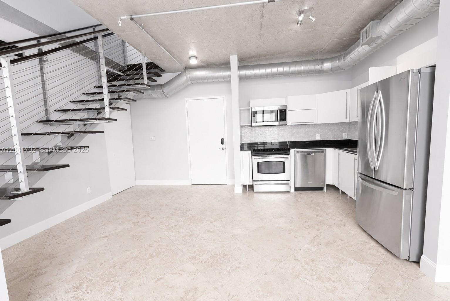 A kitchen with stainless steel appliances and a floating staircase in an industrial-style room — 690 SW 1st Ct # 3118, Miami FL 33130, MIAMI, FL