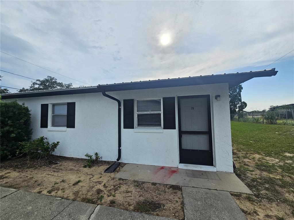 A white, single-story exterior features a black-framed screen door, two windows with shutters, and a roof — 455 S BUCKMOORE ROAD UNIT 78, LAKE WALES, FL
