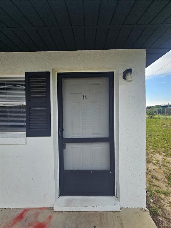 A white exterior wall features a grey front door with a screen door marked 78 — 455 S BUCKMOORE ROAD UNIT 78, LAKE WALES, FL