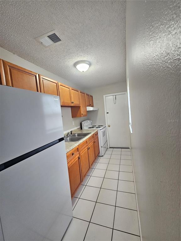 A galley kitchen features light wood cabinets, white appliances, and white tile flooring — 455 S BUCKMOORE ROAD UNIT 78, LAKE WALES, FL