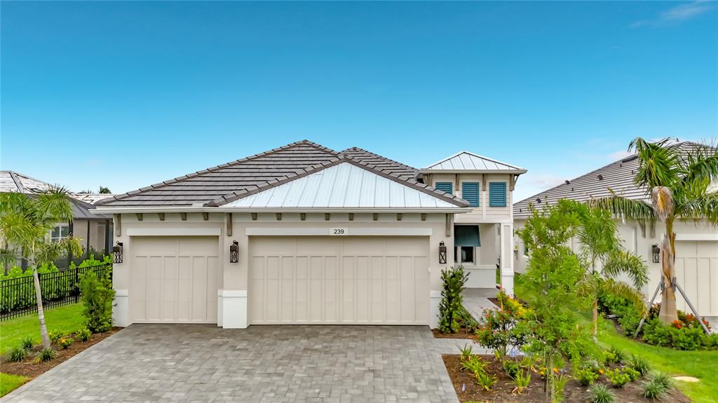 A beige single-story house with a metal roof and a paved driveway under a blue sky — 239 MONET TRAIL, BRADENTON, FL