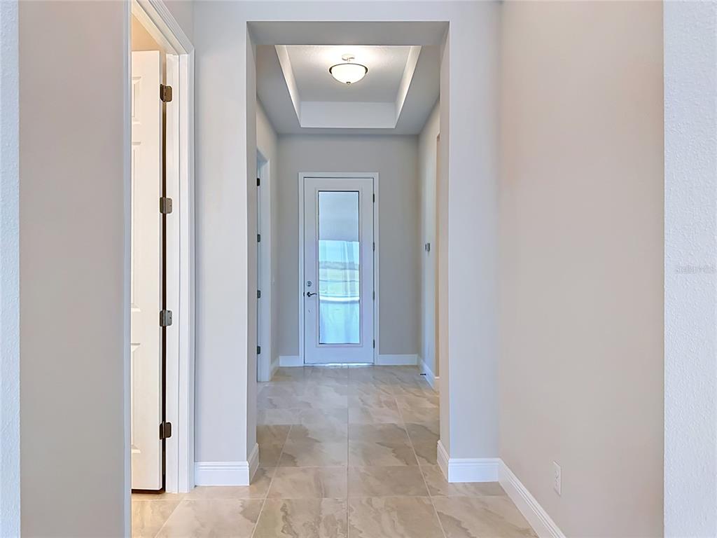 A hallway with light-colored tile flooring leads to a glass-paneled door under a tray ceiling — 239 MONET TRAIL, BRADENTON, FL