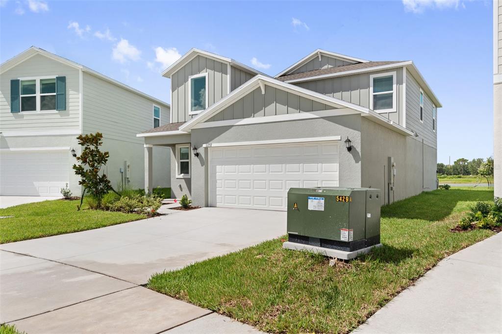 A two-story suburban house with a gray exterior, white garage door, and a green transformer — 11737 NOBLE BLOSSOM LOOP, DADE CITY, FL