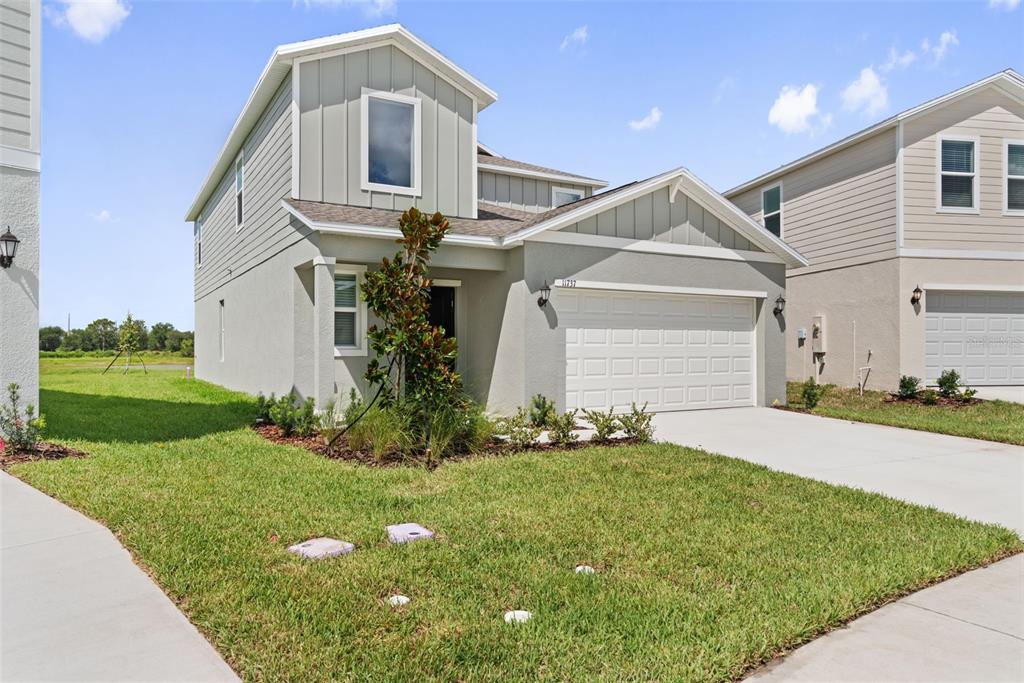 A two-story house with light green siding, a two-car garage, and a front lawn — 11737 NOBLE BLOSSOM LOOP, DADE CITY, FL