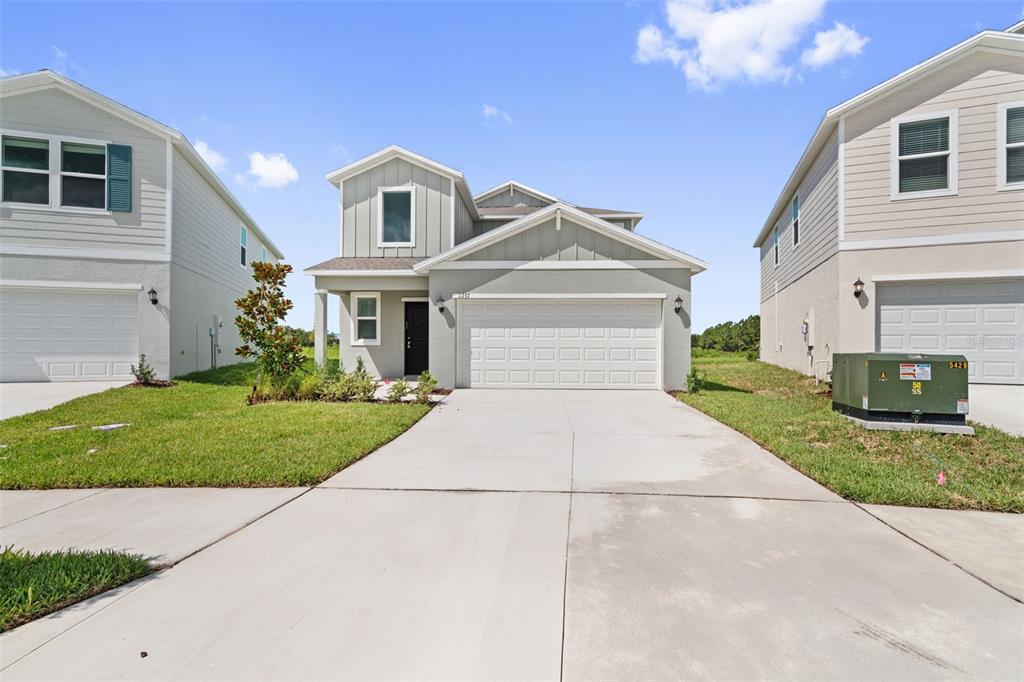 A two-story suburban house features a light gray exterior, a two-car garage, and a driveway — 11737 NOBLE BLOSSOM LOOP, DADE CITY, FL