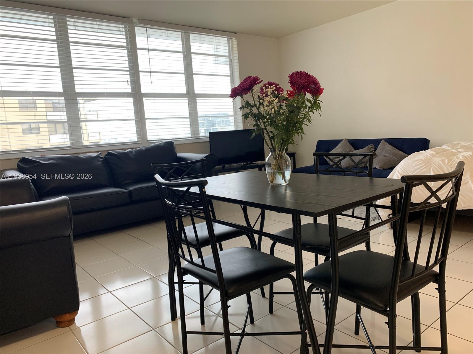 A dining set sits in a living room with tile floors, a black sofa, and blinds — 100 Lincoln Rd # 805, Miami Beach FL 33139, MIAMI BEACH, FL