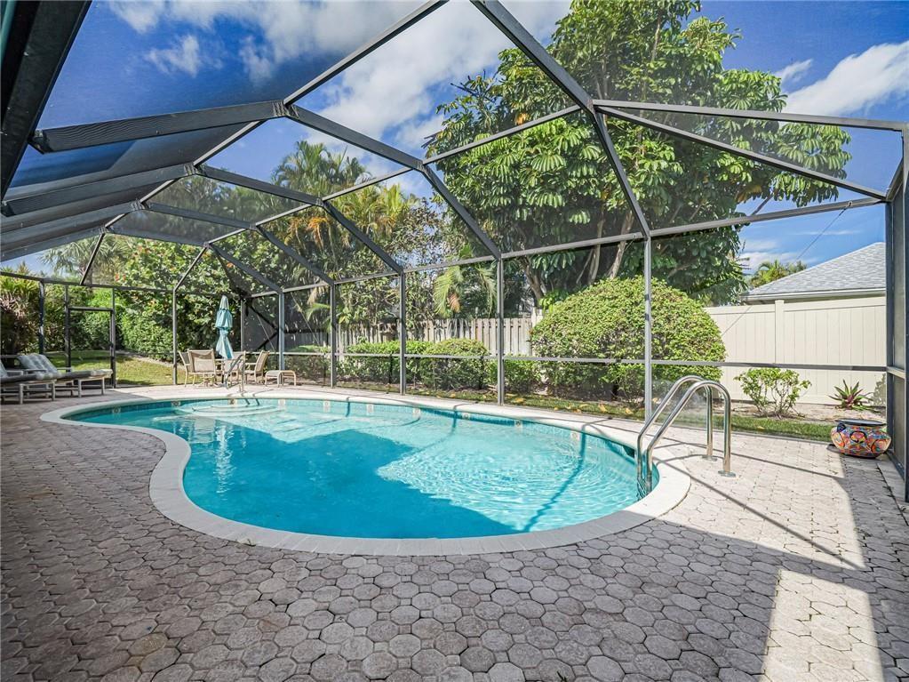 A screened-in swimming pool with a paver deck sits in a backyard with lush landscaping — 1330 Shorewinds Lane, Vero Beach FL 32963, VERO BEACH, FL