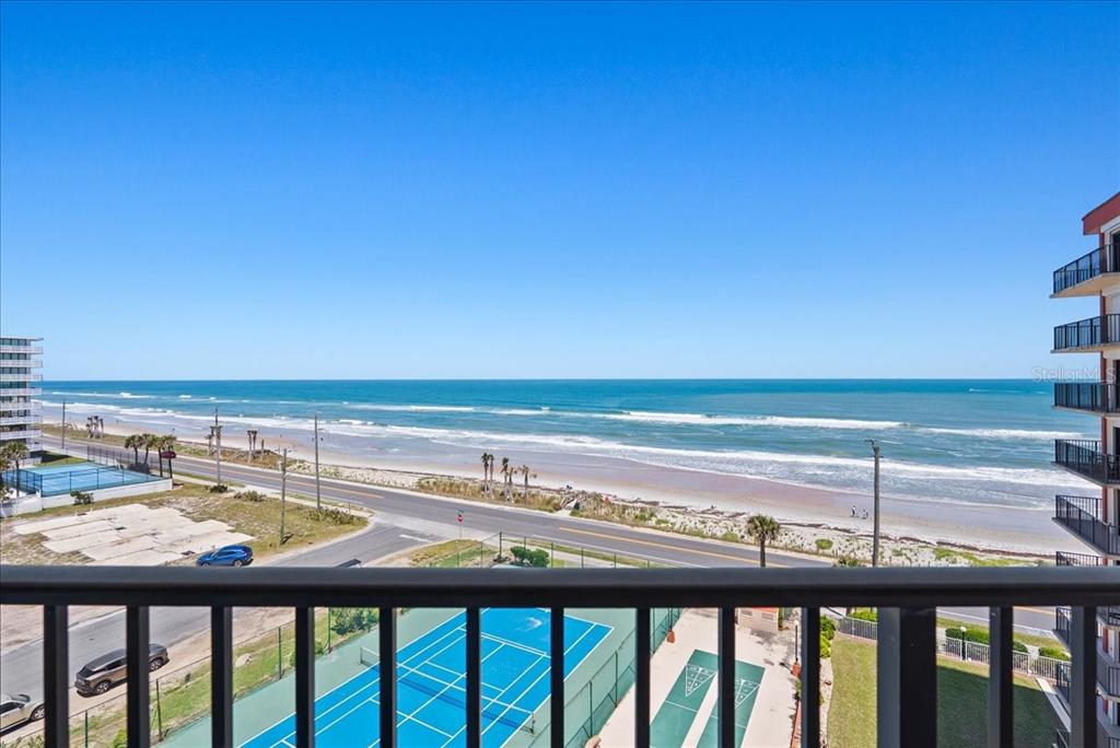 A high-angle view from a balcony overlooking a beach, a coastal road, and tennis courts — 3600 S OCEAN SHORE BOULEVARD UNIT 712, FLAGLER BEACH, FL