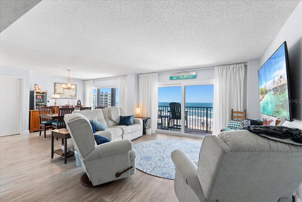 A living room with light wood floors, a balcony overlooking the ocean, and a television — 3600 S OCEAN SHORE BOULEVARD UNIT 712, FLAGLER BEACH, FL