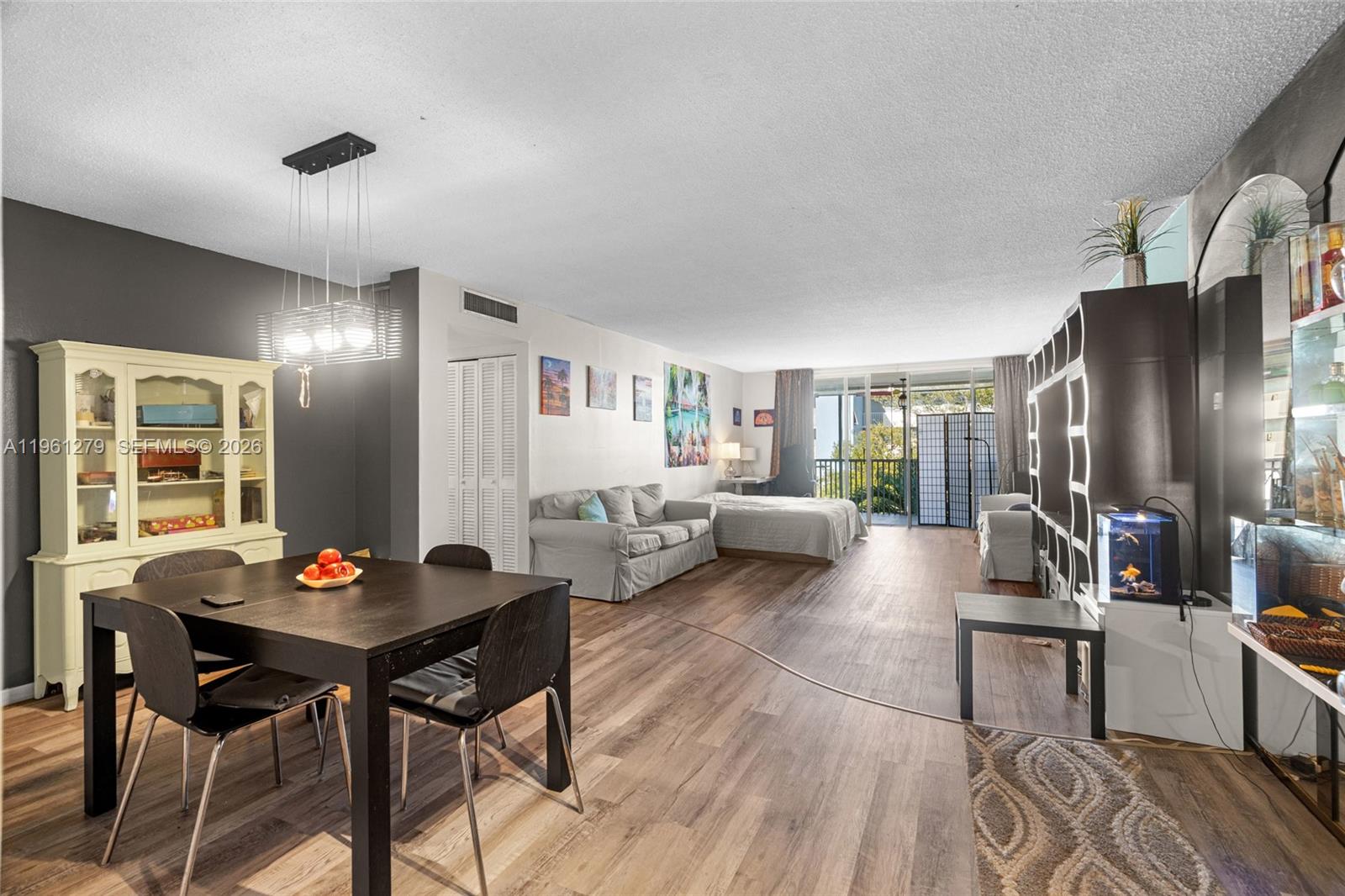 An open-concept living and dining area features wood-look flooring, a dining set, and a bed — 1690 NE 191st St # 1, Miami FL 33179, MIAMI, FL