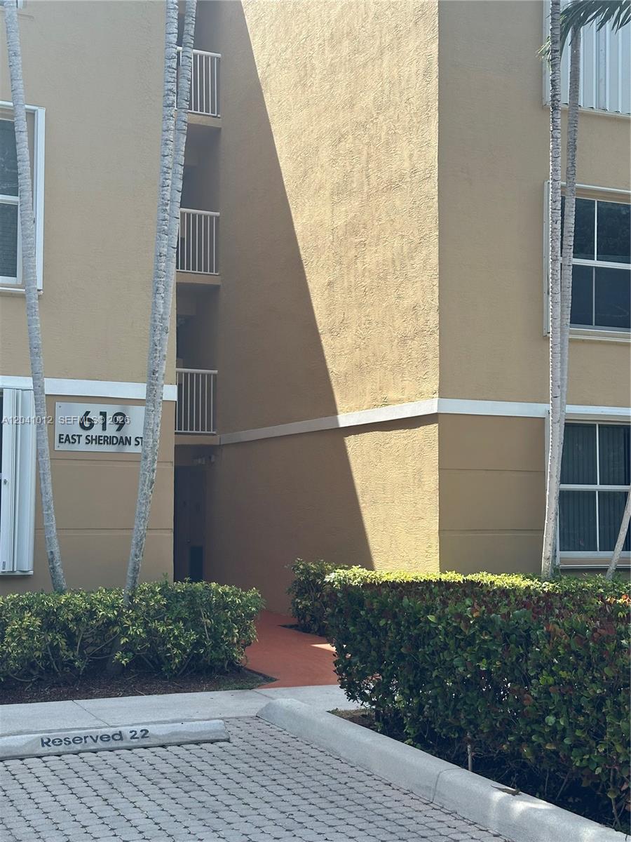 The exterior of a multi-story apartment building features a tan facade and a reserved parking space — 619 E Sheridan St # 105, Dania Beach FL 33004, DANIA BEACH, FL