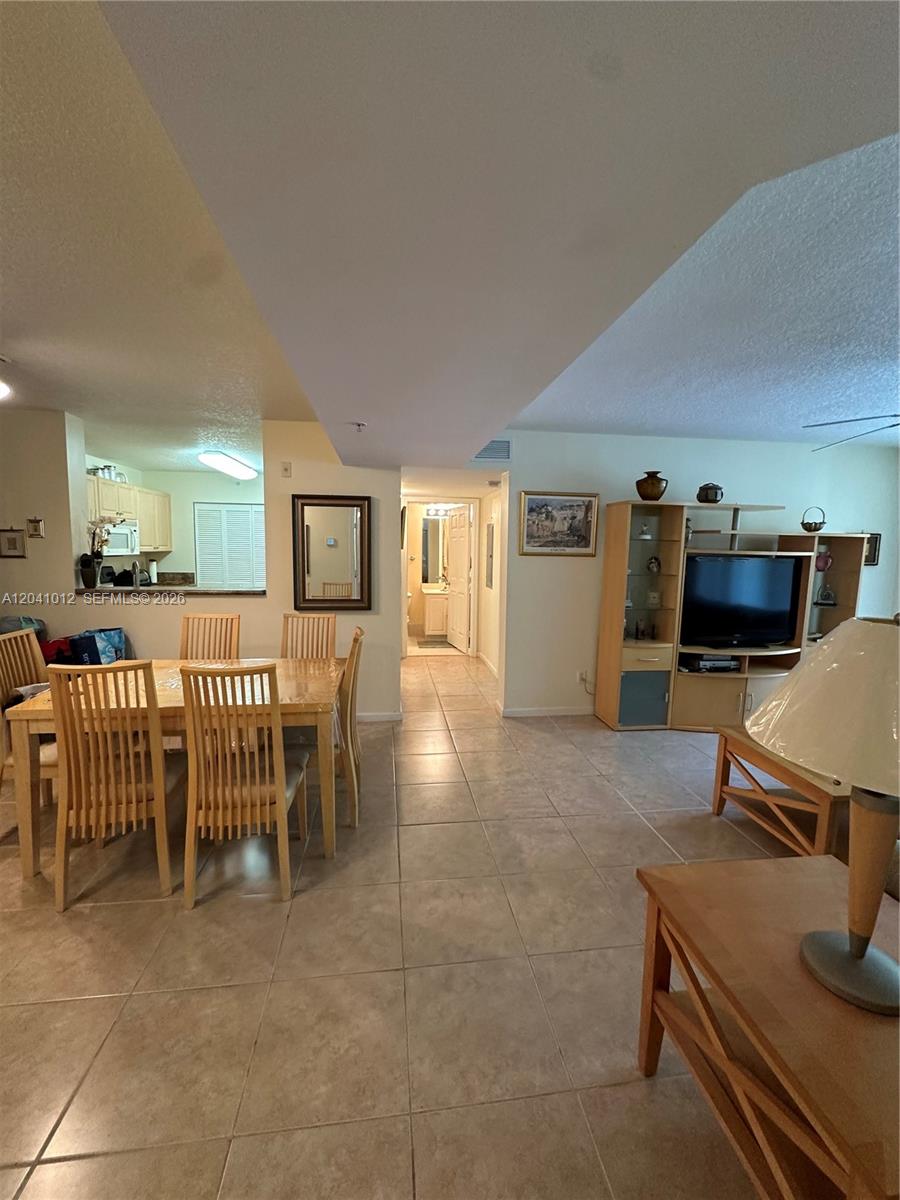 A dining area and living room with tile flooring lead to a hallway and kitchen — 619 E Sheridan St # 105, Dania Beach FL 33004, DANIA BEACH, FL