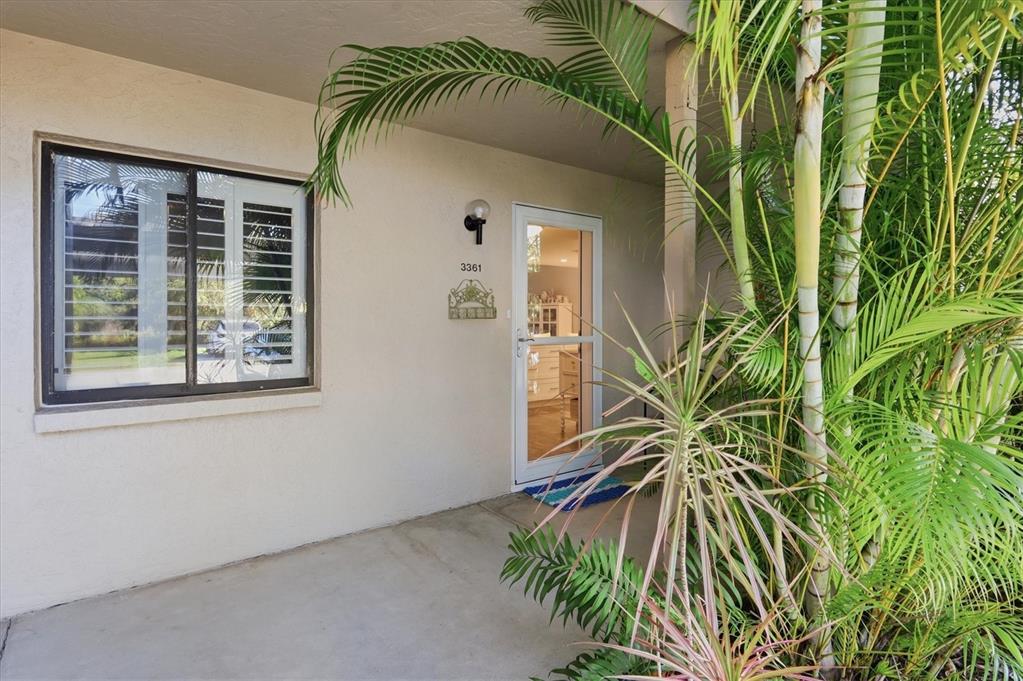 A covered entryway features a white front door, a window with shutters, and tropical plants — 3361 CROSS CREEK DRIVE UNIT 3361, SARASOTA, FL