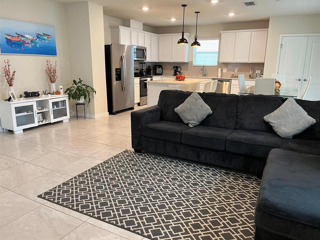An open-concept living room and kitchen feature tile flooring, a dark sectional, and white cabinetry — 893 RIVERS CROSSING STREET, CLERMONT, FL