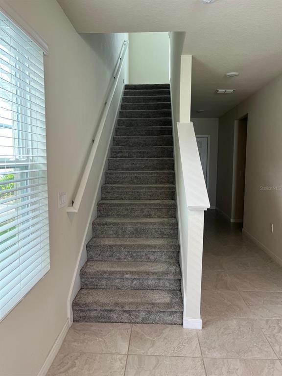 A carpeted staircase with a white railing leads to an upper level in a hallway — 893 RIVERS CROSSING STREET, CLERMONT, FL
