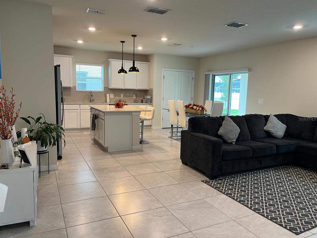An open-concept kitchen, dining area, and living room featuring tile floors and white cabinetry — 893 RIVERS CROSSING STREET, CLERMONT, FL