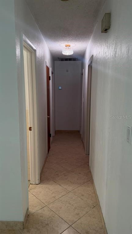 A narrow hallway with light-colored tile flooring leads to a doorway at the end — 6412 N WOODLYNNE AVENUE, TAMPA, FL