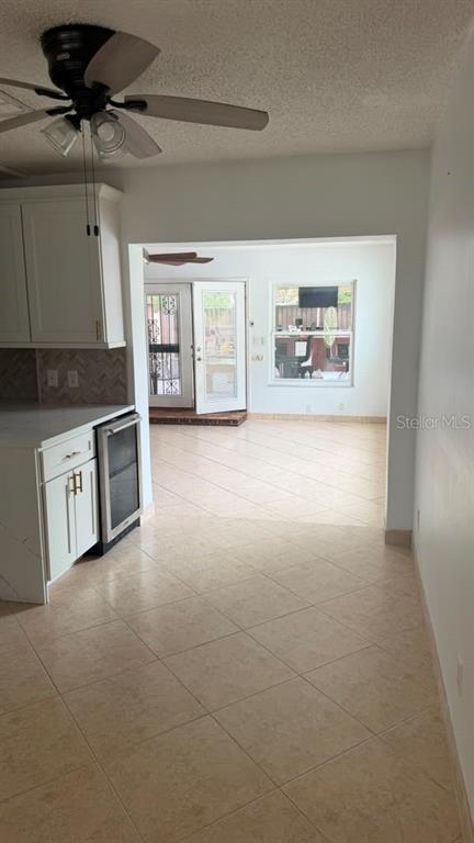 A kitchen with white cabinets and tile flooring opens into a sunlit living area — 6412 N WOODLYNNE AVENUE, TAMPA, FL