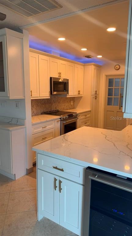 A kitchen features white cabinets, quartz countertops, a stainless steel oven, and blue accent lighting — 6412 N WOODLYNNE AVENUE, TAMPA, FL