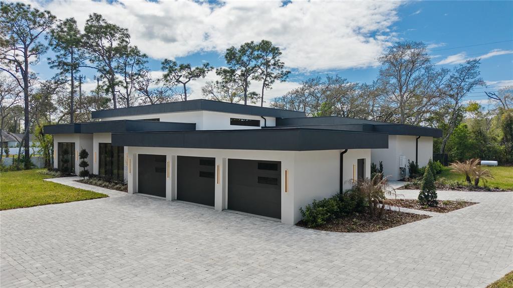 A modern, flat-roofed house features a three-car garage and a paved driveway — 1447 BIRD ROAD, WINTER SPRINGS, FL